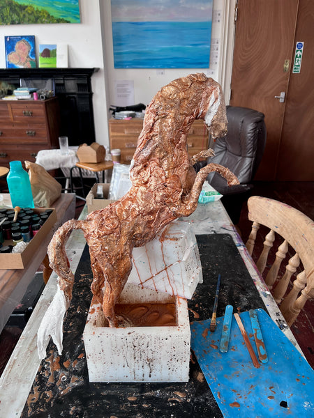 The Queen of Sheba in progress, with a textured copper-coloured body and raised forelegs, supported on a studio workbench as the resin is poured over the sculpture.