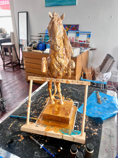 Front view of The Queen of Sheba during making, showing the gold-coloured horse with raised forelegs behind a wooden support.
