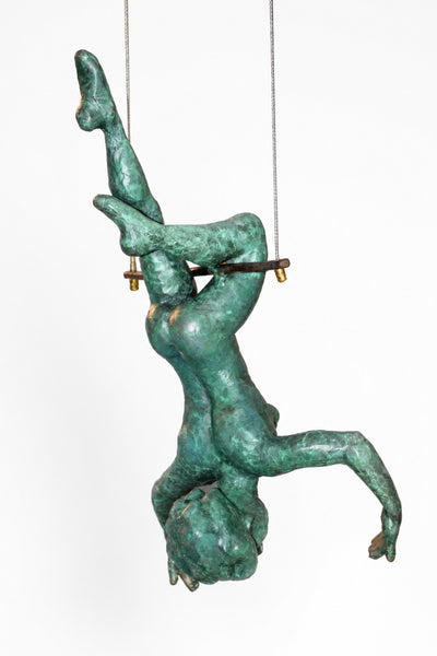 A green patina bronze sculpture of a human figure suspended upside down by a horizontal bar, set against a plain white background.