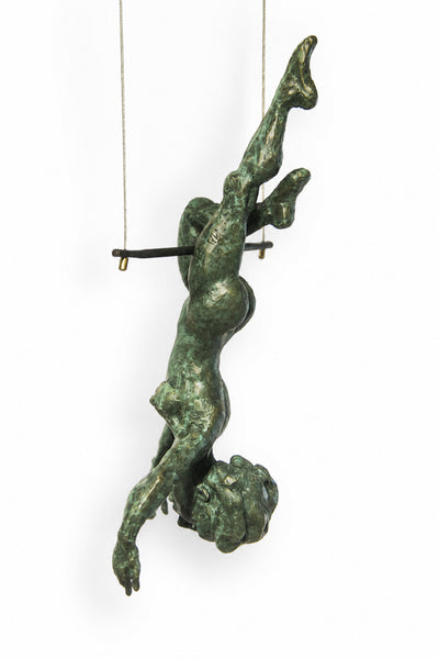 A green patina bronze sculpture of a human figure suspended upside down from a horizontal bar, with thin wires extending to the top of the frame, set against a plain white background.