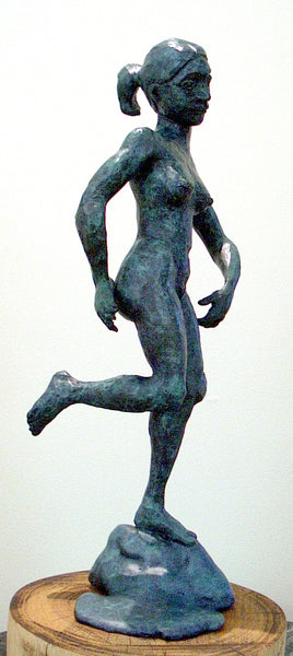 Bronze sculpture of a nude female figure in a running pose, mounted on a rock base and displayed on a round wooden pedestal against a plain light background.