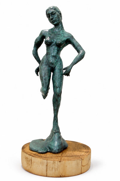 A bronze sculpture of a standing nude female figure with a green patina finish, mounted on a round natural wood base, shown against a plain white background.