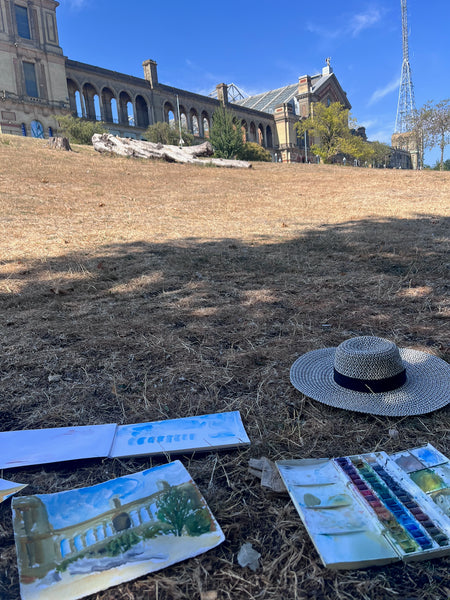 Watercolour study, sketchbook, paint palette and sunhat on dry grass during Stephanie Fuller’s plein air painting session at Alexander Palace.