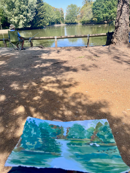 Stephanie Fuller’s pond painting held beside the scene it depicts, with trees, waterbirds and an angler on the bank.