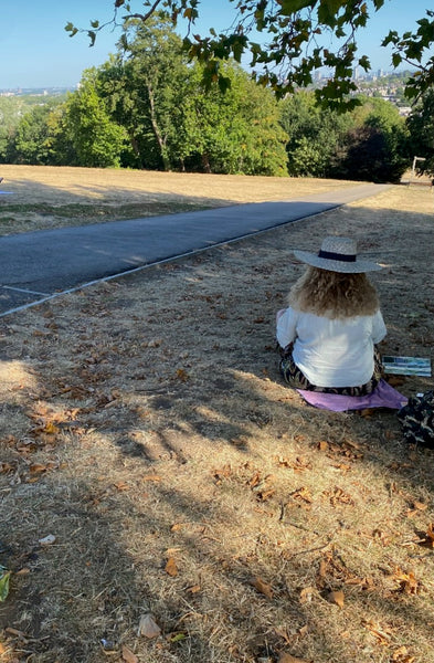 Stephanie Fuller seated beneath trees at Alexander Palace, painting the view across the grassy slope towards London.